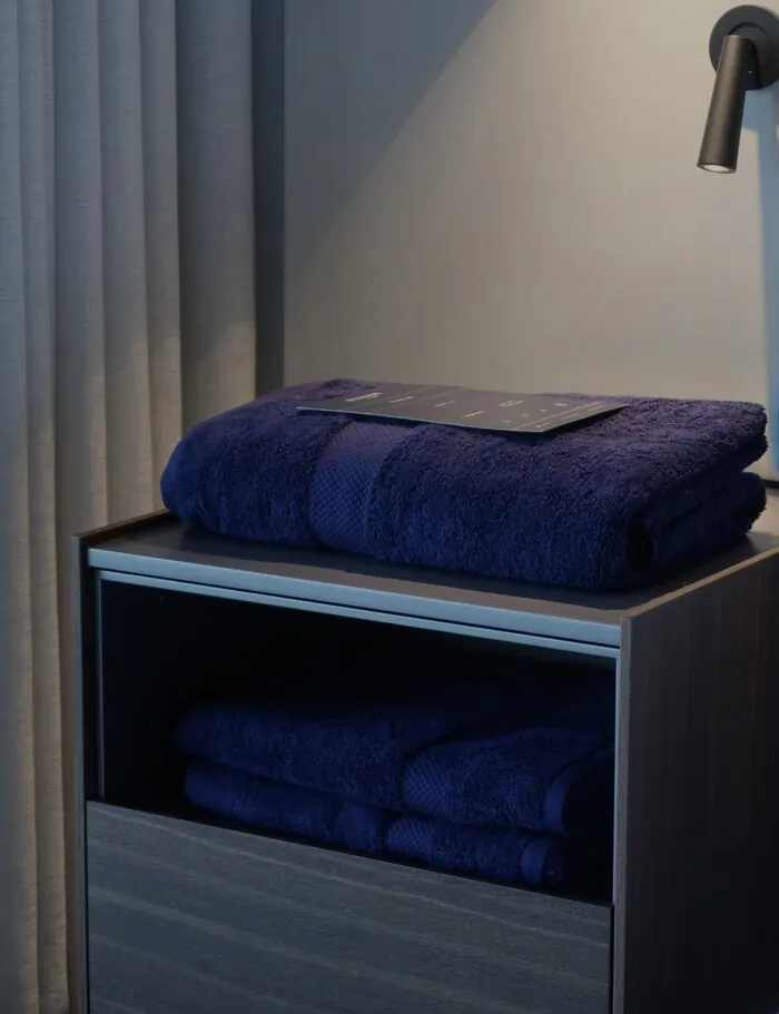 Juego de toallas BYROSH azul marino en la mesita de una habitación de hotel